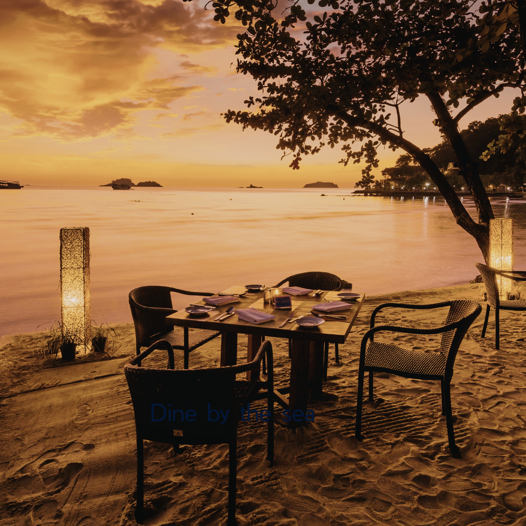 Group of people dining by the sea, laughing and enjoying a meal together with the ocean in the background